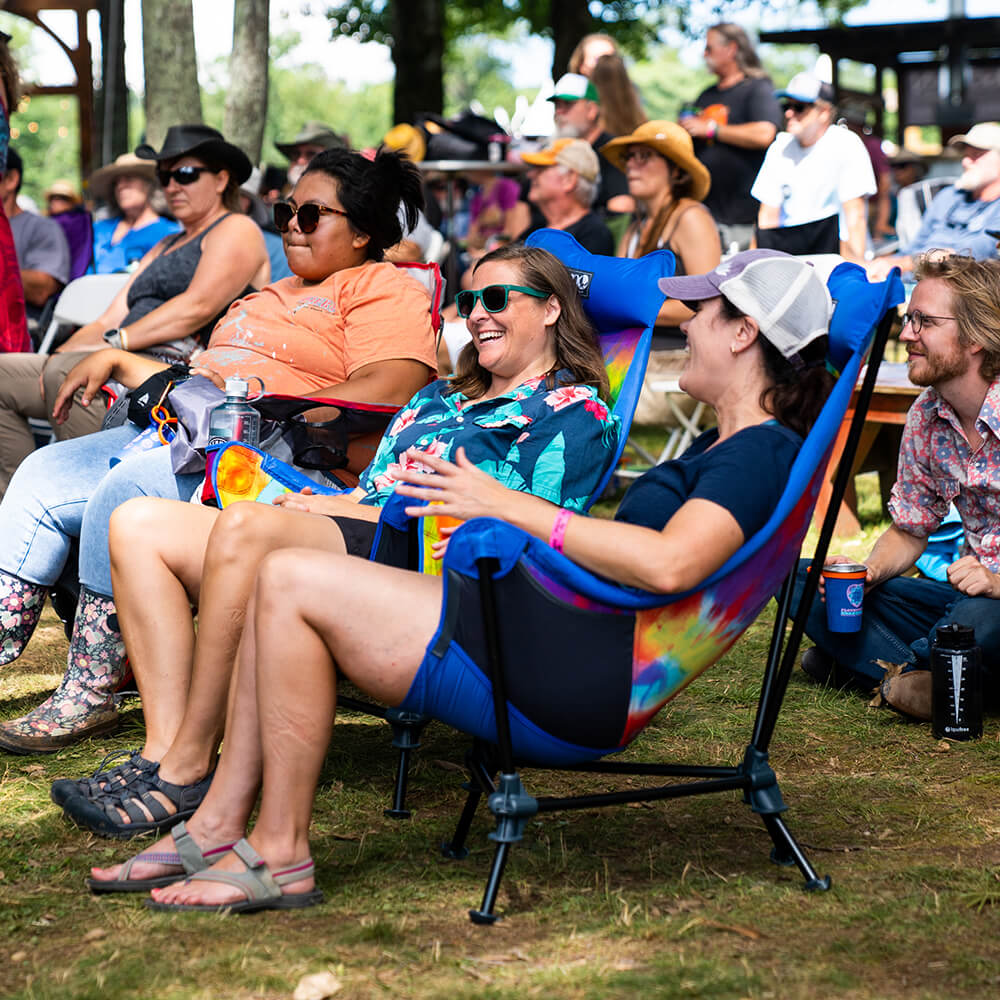 Two women sit smiling amongst a busy audience in the ENO festival chair.