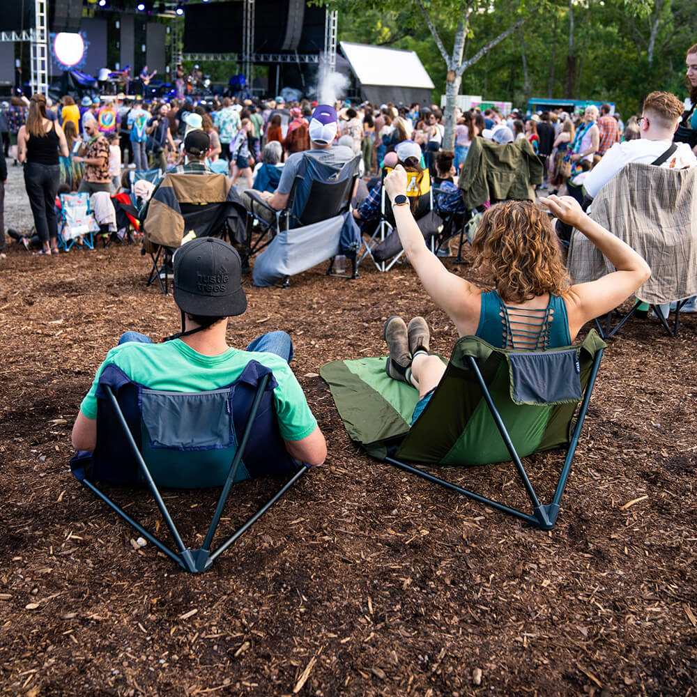 A couple sits amongst an audience at a music gathering on packable ENO ground chair.