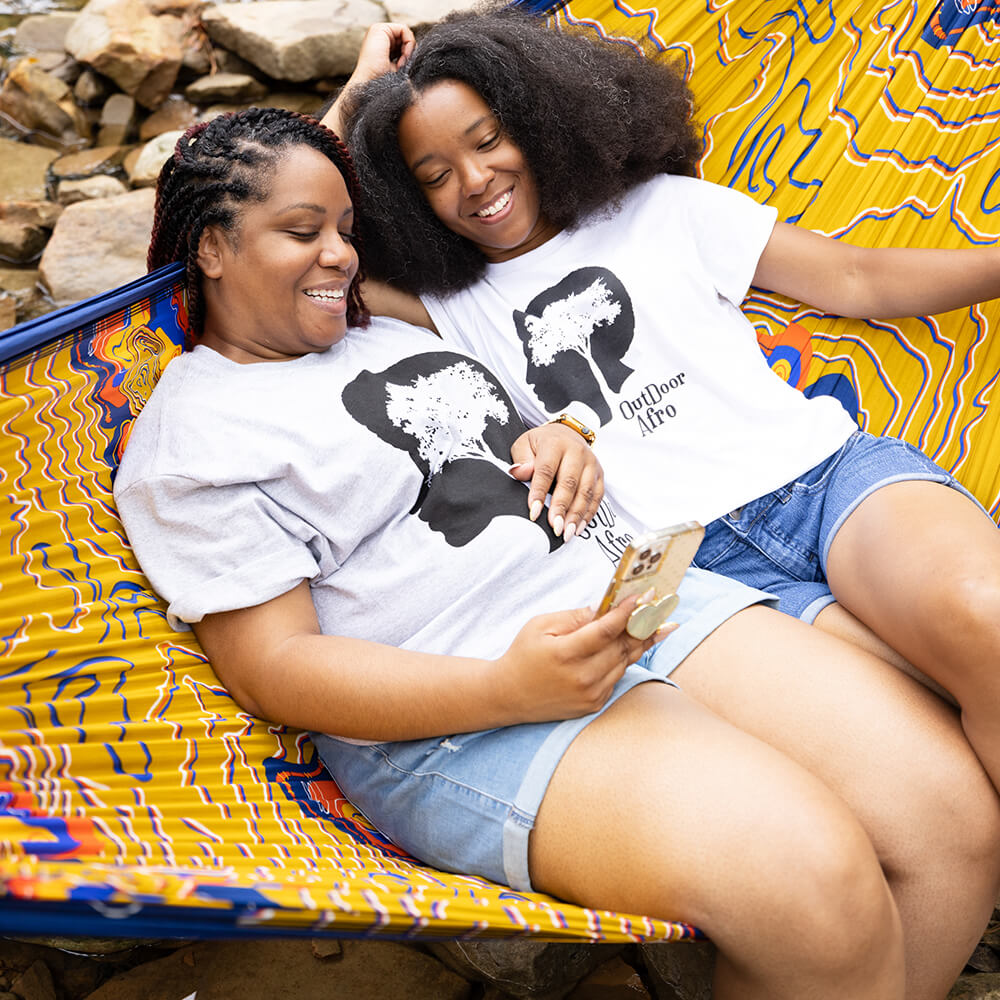 Two women sitting in an ENO giving back hammock looking at a cell phone.