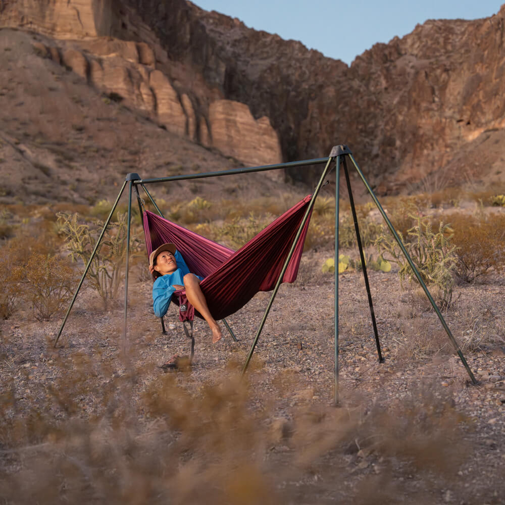 A person lays back in their DoubleNest Hammock attached to a ENO Nomad Hammock Stand in the backcountry.