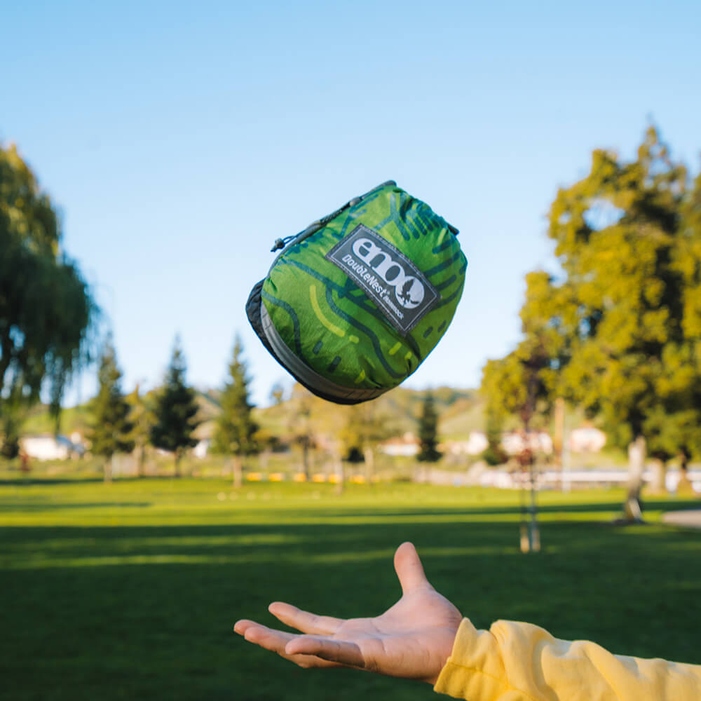 A person tossing a packed ENO hammock in the park with their hand below.