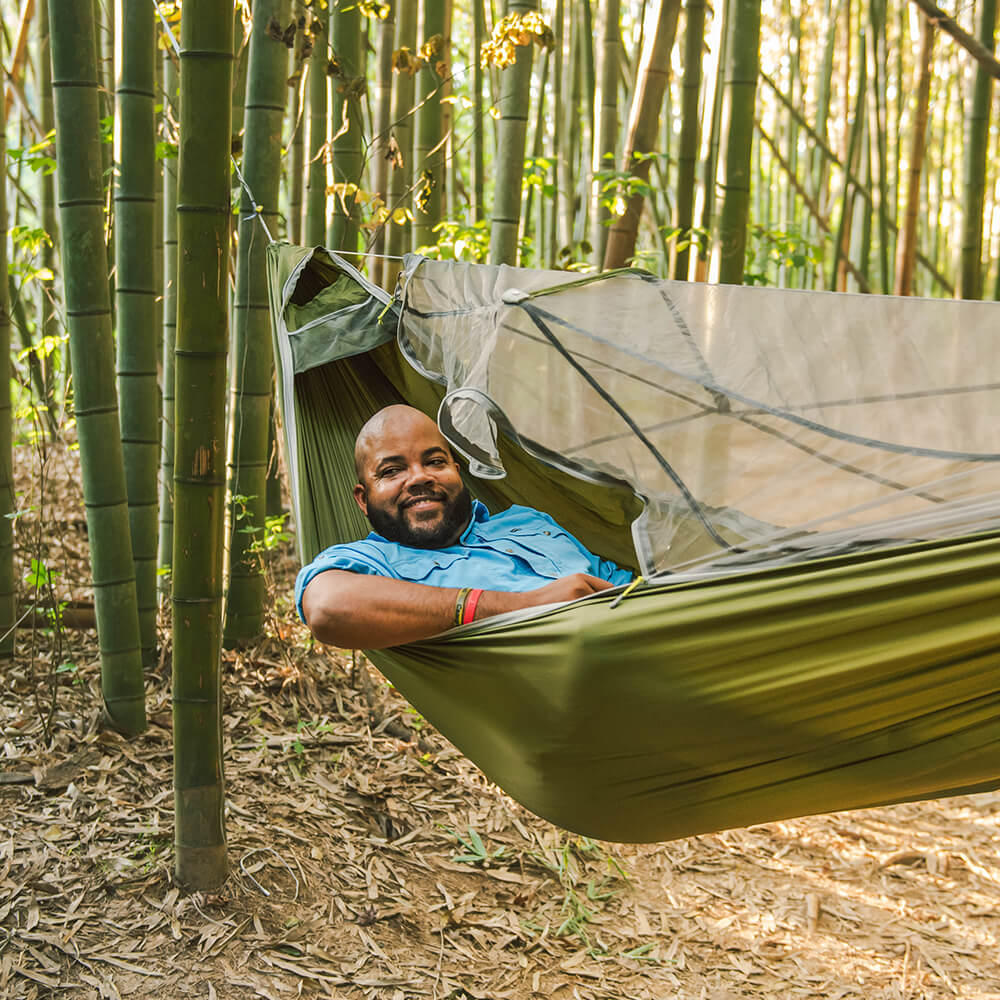 A person looks off camera, smiling, while laying back in their ENO JungleLink Hammock System.