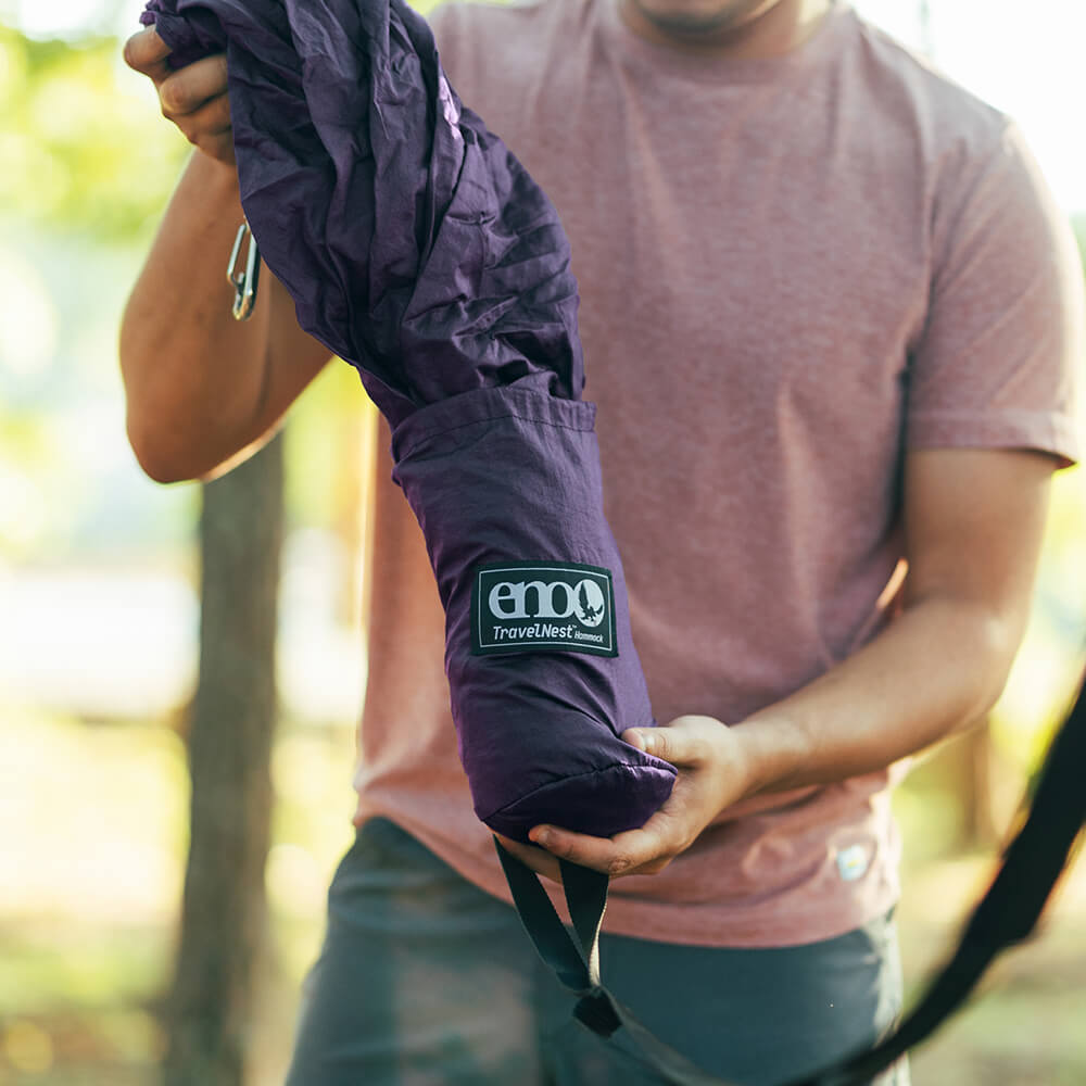 A person pulling a plum ENO portable hammock out of the stuff sack with a hammock strap in hand.