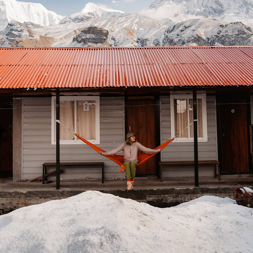 A person sitting in an ENO portable hammock with snow in the foreground and snowy mountains in the background.