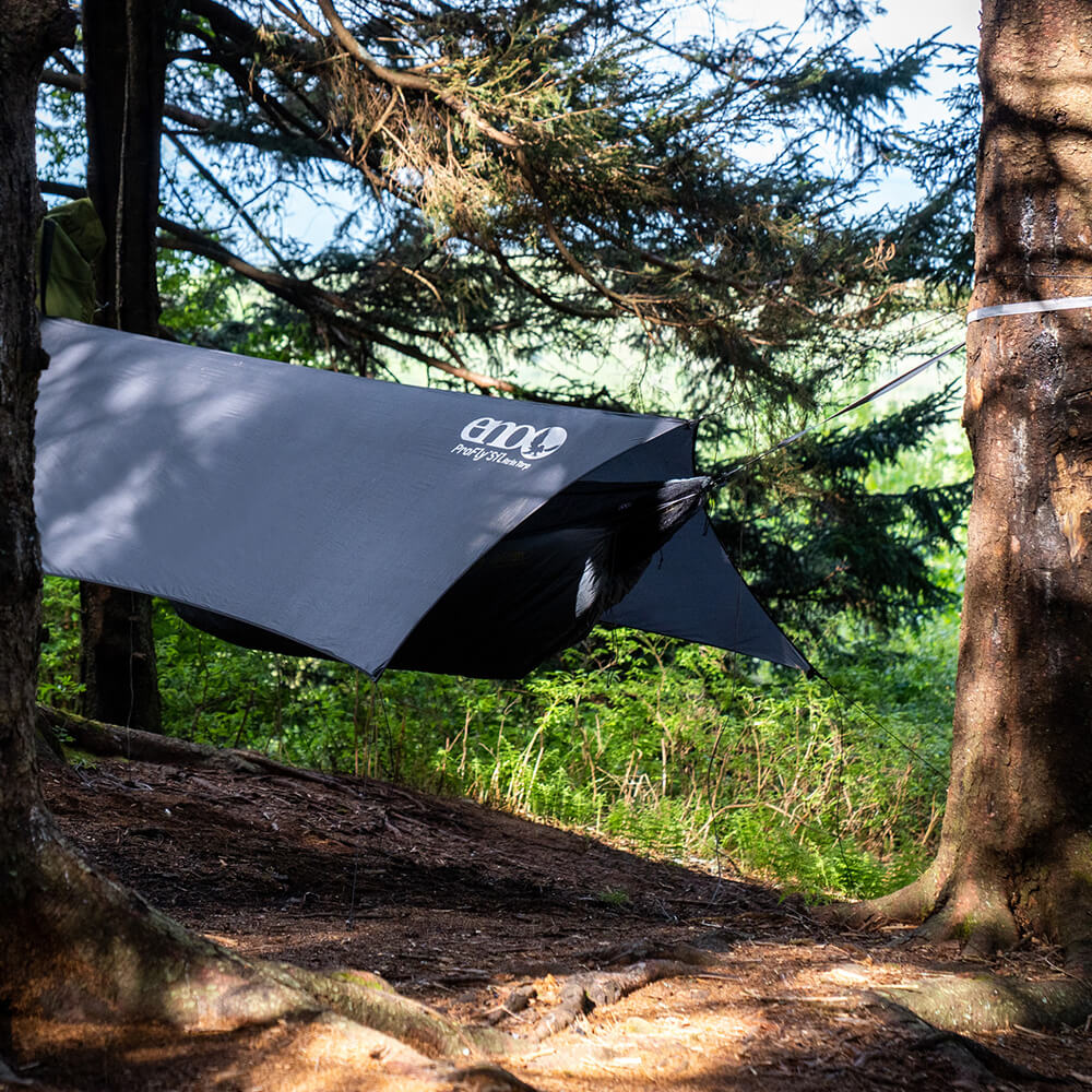 ENO ultralight hammock tent consisting of hammock, bug net, and rain tarp set up between trees in woods.